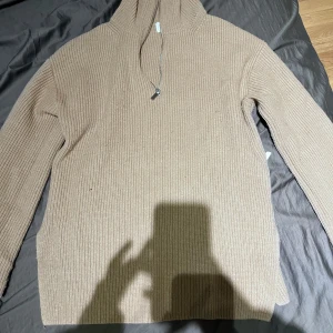 Beige ribbad hoodie från H&M - Säljer en beige ribbstickad hoodie från H&M i storlek S. Tröjan har huva med snörning, långa ärmar och är tillverkad i ett mjukt stickat material. Perfekt för lager-på-lager och chill dagar.