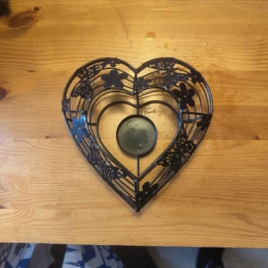 Hjärtformad ljushållare  -  hjärtformad ljushållare i metall med blommönster, avsedd för ett värmeljus. Produkten är i gott skick utan synliga defekter eller slitage.