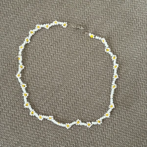 Pärlhalsband med blommor i vitt och gult - Supergulligt halsband gjort av små pärlor i vitt och gult, formade som små blommor längs hela kedjan. Halsbandet är 42cm långt 🤍💛