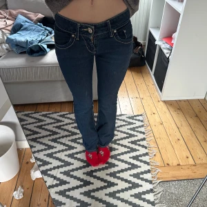 Mörkblå Evisu jeans med broderade fickor - Säljer ett par mörkblå Evisu jeans med snygga kontrastsömmar och broderade bakfickor. Modellen har låg midja och raka ben med lätt bootcut. Jeansen är tillverkade i klassiskt denim och har detaljer som metallknappar och logotyp på insidan.