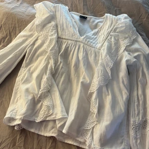 Vit blus med volanger från Gina Tricot - Supersöt vit blus från Gina Tricot i storlek XS. Blusen har v-ringning, långa ärmar och fina volangdetaljer med spets längs framsidan och ärmsluten. Använd 1 gång köpte för 499kr❤️