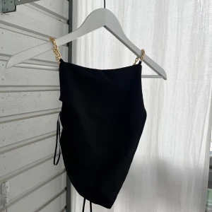 Svart fest topp med guldkedjor från Zara - Supersnygg svart fest topp från Zara med guldfärgade kedjor som axelband och cool snörning i ryggen. Aldig använd! Står storlek L på etiketten men är en S!