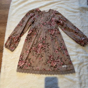 Blommig långärmad klänning från Newbie - Supersöt beige klänning från Newbie med rosa och vinröda blommor, långa puffärmar och spetskant nertill. Klänningen har en mjuk och skön känsla, perfekt för dig som gillar romantiska vibes och vintageinspirerat. Rund halsringning och avslappnad passform. Klänningen är i jättebra skick förutom några fläckar framsidan vänster, de syns enbart om man tittar väldigt nära, smälter annars in i mönstret på klänningen 