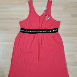 Röd Snoopy sovplagg med brodyr XL - Superfin röd sovplagg från Snoopy i 100% bomull. Den är ärmlös med v-ringning, har broderade blommor och Snoopy-tryck på bröstet samt ett svart bälte med blommönster i midjan. Perfekt för dig som vill ha något färgglatt och bekvämt!