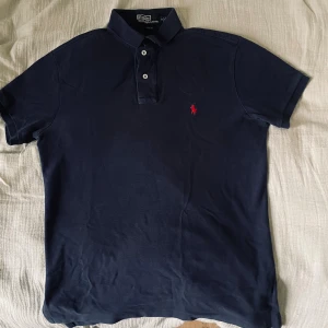 Mörkblå piké från Ralph Lauren  - Klassisk piké från Ralph Lauren i mörkblått med röd broderad logga. Snygg slim fit-look som alltid funkar – både till vardags och lite mer uppklätt.  📏 Storlek: S ✨ Skick: Bra skick, använd men välvårdad. 🧵 Material: Bomull – skön och sval, perfekt året runt.                                                                                        ✅ Pris kan diskuteras