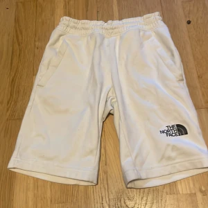Vita shorts från The North Face - Snygga vita shorts från The North Face med elastisk midja och två fickor. STORLEKEN ÄR JUNIOR MEDIUM INTE VANLIG MEDIUM! Stora loggor på både framsidan och längs benet ger en sportig vibe. Perfekta för sommardagar och chill häng. Materialet känns mjukt och bekvämt, troligtvis polyester.