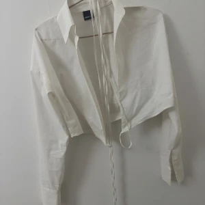 Vit croppad skjorta med snörning Gina Tricot - Säljer en vit croppad skjorta från Gina Tricot med långa ärmar och snygg snörning framtill. Skjortan har klassisk krage och knappar vid ärmsluten. Perfekt för en trendig och stilren look. Storlek 34, endast använd två tillfällen. 