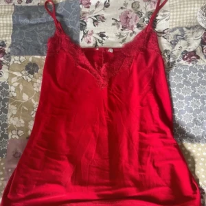 Röd linnetopp med spetsdetaljer -  Snygg röd linnetopp med tunna axelband och v-ringning dekorerad med spets. Toppen har en mjuk och följsam känsla, perfekt för att lyfta vilken outfit som helst. Enkel att matcha och ger en trendig vibe.