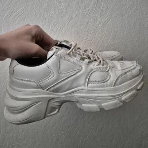 Chunky vita sneakers i storlek 38 - Chunky vita sneakers med kraftig sula och snörning. Skorna har en modern och sportig design med detaljer i vitt och beige. Ovandelen är i syntetmaterial och insidan är svart. Perfekta för dig som gillar streetstyle och vill ha en cool look. 