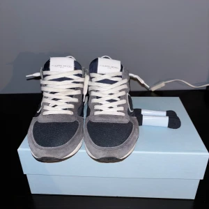Philippe Model sneakers i mörk grå och marinblå - Snygga Philippe Model sneakers i mörk grå mocka och marinblå textil med vita detaljer och snörning. Klassisk sportig siluett med rund tå och platt sula. Kommer med extra marinblåa skosnören och originalkartong. Skorna är i mycket gott skick och knappt använda.