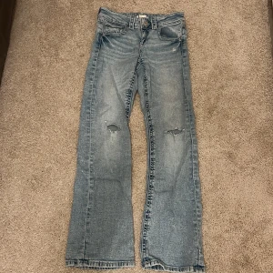 Blå bootcut jeans från Gina Tricot - Snygga ljusblå jeans från Gina Tricot i storlek 152. Modellen är bootcut med slitningar på knäna och tjusiga fickor, vi hittade ett hål bak vid höger ficka men som nu är lagat med stark tråd!