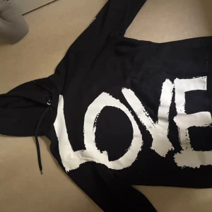 Svart Burberry hoodie  - Svart hoodie från Burberry med stort vitt LOVE-tryck på framsidan och Burberry London England-logga på axeln. Tröjan har huva med snörning och är tillverkad i mjuk bomull. Är tidigare använd bara en gång av min farsa.