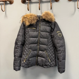 Svart pufferjacka Rockandblue med fuskpäls - Snygg svart pufferjacka från Rockandblue med stor fuskpäls på huvan och guldiga dragkedjor. Jackan har quiltade detaljer, flera fickor med dragkedja och Rockandblue-logga på ärmen. Ej använd mycket, nypris ca 5000!!💗✨