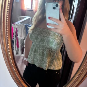 Grön blommig tubtopp från Gina Tricot - Säljer en söt grön tubtopp från Gina Tricot i storlek S. Toppen har ett vitt blommigt mönster, smockad överdel och volang nedtill. Perfekt för varma dagar och enkel att styla med jeans eller kjol. Superfin färg och skön passform!