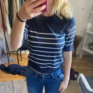 Mörkblå randig stickad tröja - Säljer en mörkblå stickad tröja med vita horisontella ränder. Tröjan har rund halsringning och halvlånga ärmar, vilket ger en chill och stilren vibe. Perfekt till jeans eller kjol för en enkel men snygg look.