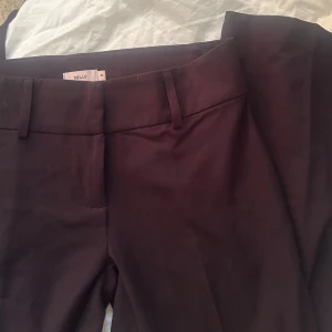  kostymbyxor från Nelly - Snygga mörkbruna kostymbyxor från Nelly med klassisk rak passform och hällor för bälte. Perfekta för en stilren look och enkla att matcha med olika toppar. Byxorna har en tidlös design och är tillverkade i ett mjukt material som känns bekvämt hela dagen.