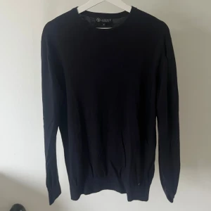 Marinblå stickad tröja från Therlunds - En stilren marinblå stickad tröja från Therlunds egna märke ”Lagency” i storlek M. Tröjan har rund halsringning, långa ärmar och ribbade muddar vid ärmslut och nederkant. Perfekt för lager-på-lager och enkel att matcha med olika outfits.