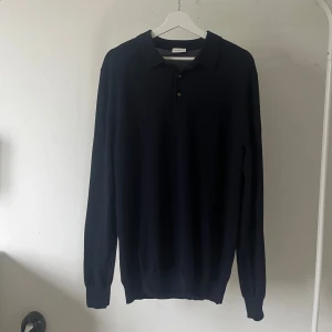  pikétröja i kashmir  - Klassisk marinblå långärmad pikétröja från John Henric. Tröjan har krage, knappar framtill och ribbade muddar vid ärmslut och nederkant. Perfekt för en stilren och clean look. Modellen är 180cm