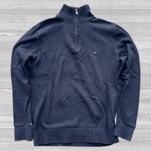 Mörkblå half zip tröja Tommy Hilfiger - Mörkblå långärmad tröja från Tommy Hilfiger i premium bomull. Tröjan har en stilren half zip-dragkedja vid halsen och diskret broderad logga på bröstet. Perfekt för dig som gillar klassisk och clean stil. Storlek S, passar XS
