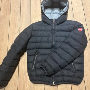 Mörkblå Colmar vinterjacka med huva - Mörkblå vinterjacka från Colmar med huva och två dragkedjeförsedda fickor.  Ej den allra varmaste modellen.            Jackan har quiltad design, logotyp på ärmen och nederkanten samt hel dragkedja framtill. Perfekt för kalla dagar och riktigt snygg streetstil.           Dragkedjan trasig, därav det låga priset, se sista bilden. Nypris ca 5000kr