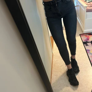 Svarta skinny jeans med råa benslut - Säljer ett par svarta skinny jeans med hög midja och råa benslut. Jeansen är tighta och sitter snyggt längs benen. Klassisk femficksmodell i stretchigt jeanstyg som ger en schysst passform. Perfekta för dig som gillar en clean och stilren look.