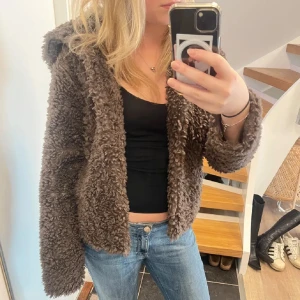 Brun teddyjacka  - Mysig brun teddyjacka med huva och fluffig struktur. Jackan är croppad och har en avslappnad passform med långa ärmar. Perfekt för kyliga dagar när du vill vara både varm och snygg. Hör av dig vid frågor🥰