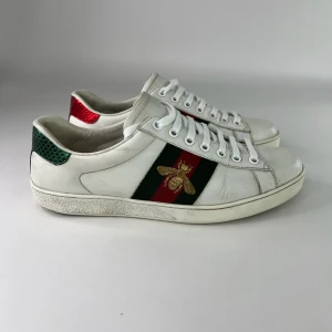 Gucci Ace vita sneakers med bi - Gucci Ace sneakers i vitt skinn med klassiska gröna och röda ränder på sidorna och broderad guldfärgad bi.