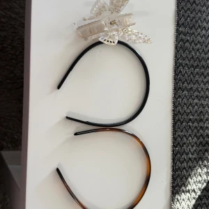 2 diadem och en fjärilshårklämma - Säljer två smala diadem i plast, ett helsvart och ett i brunmelerad sköldpaddsfärg. Medföljer gör en liten transparent hårklämma i form av en fjäril med glittriga detaljer. Perfekt för att fixa frisyren snabbt och snyggt.