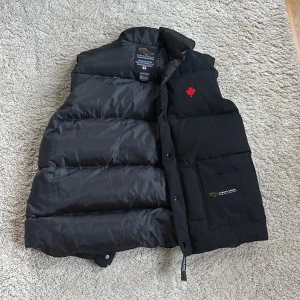 Väst från Canada Goose  - Säljer en svart dunväst från Canada Goose i storlek L. Västen är helt äkta, och har inga defekter/skador . på bröstet finns ett rött lönnlöv broderat. Perfekt för kyliga dagar nu i höst och vinter😄❄️