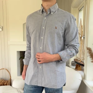 Grå skjorta från Ralph Lauren M - Klassisk grå skjorta från Ralph Lauren med button-down krage och broderad logga på bröstet. Skjortan har lång ärm, vita knappar och är tillverkad i mjuk bomull. Perfekt för en clean och stilren look.