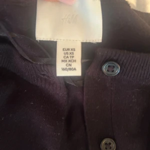 Mörklila kofta från H&M XS - Säljer en mörklila kofta från H&M i storlek XS. Koftan har knappar framtill, ribbade muddar vid ärmslut och nederkant samt långärmad passform. Perfekt att slänga över en topp för en chill och snygg look.