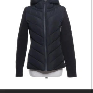 Svart jacka  från Zara - Svart jacka från Zara med snyggt chevronmönster på framsidan och huva. Jackan har långa ärmar och dragkedja framtill. Perfekt för kyliga dagar och har en stilren, modern look som passar till många outfits. Använd några gånger.