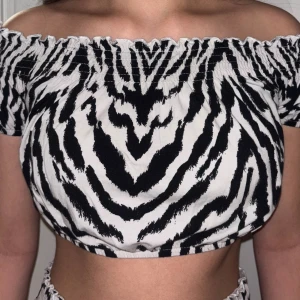 Zebramönstrad offshoulder topp Gina Tricot - Säljer en snygg offshoulder topp från Gina Tricot i storlek M. Toppen har ett svartvitt zebramönster, är croppad och har elastisk smock upptill och nedtill för en skön passform. Perfekt för dig som gillar djurmönster och vill sticka ut.