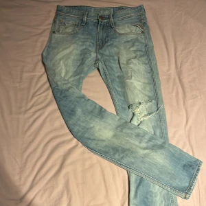Replay Anbass ljusblå jeans, W29 L32 - Säljer ett par Replay Anbass jeans i ljusblå tvätt med slitningar och trasig detalj vid knät. Klassisk femficksmodell med raka ben och snygga sömmar bak. Perfekt passform och cool faded look. Jeansmaterial med dragkedja och knapp.