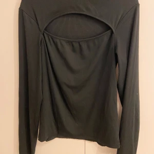Svart långärmad topp med öppen framdel - Snygg svart långärmad topp med ribbad struktur och en cool öppen fram-detalj. Toppen har en rundad halsringning och är figurnära i modellen. Perfekt för dig som vill ha en stilren men ändå unik look. Storlek är M och är från newyorker, extremt skönt matrial.
