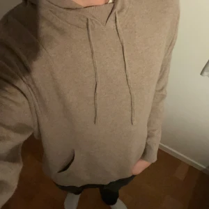 Beige kashmirhoodie från Massimo Dutti - Säljer en supermjuk beige hoodie från Massimo Dutti i 100% kashmir. Tröjan har huva med snörning och en klassisk känguruficka framtill. Perfekt för dig som vill ha en stilren och lyxig look med maximal komfort.