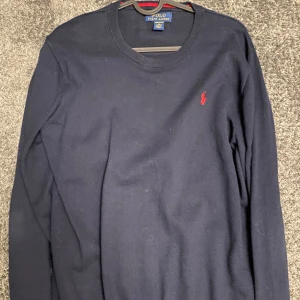 Mörkblå tröja från Polo Ralph Lauren - Mörkblå långärmad tröja från Polo Ralph Lauren i mjuk pima-bomull. Klassisk rund halsringning och röd broderad logga på bröstet. Perfekt för dig som gillar stilrena och tidlösa plagg med en sportig touch. Bara att höra av sig vid minsta funderingar🙌🌟