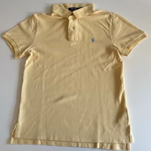 Gul pikétröja Polo Ralph Lauren - Snygg gul pikétröja från Polo Ralph Lauren i slim fit-modell. Klassisk krage, korta ärmar och knäppning framtill. Broderad blå logga på bröstet. Tillverkad i mjuk bomull som känns skön mot huden.