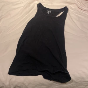 Svart linnetopp från Club XPRS - Svart enkel linnetopp från Club XPRS i storlek M. Modellen är ärmlös med klassisk rund halsringning och mjukt bomullsmaterial. Perfekt för att styla med jeans eller shorts under varma dagar.