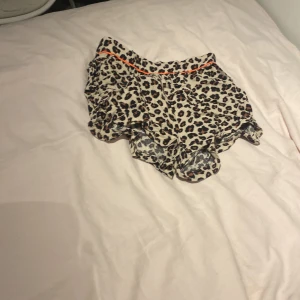 Leopardmönstrade shorts med volang - Snygga shorts med leopardmönster och volangkant. De har en beige bas med svarta och bruna fläckar samt en tunn orange linje i midjan som extra detalj. Perfekta för dig som vill sticka ut lite extra i sommarvärmen.