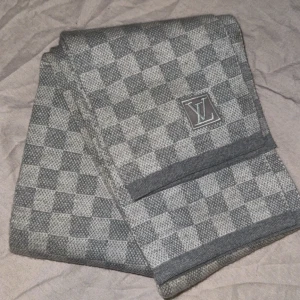 Louis vuitton halsduk damier grå - Snygg halsduk från Louis Vuitton i klassiskt rutigt mönster med LV-logga. Färgen är grå och ljusgrå, och materialet är en mjuk stickad ullblandning. Perfekt accessoar för att lyfta din outfit med en exklusiv touch. Kvittt finns