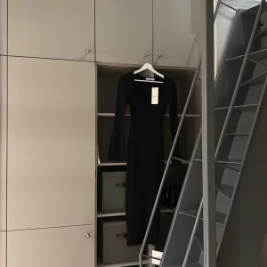 Svart långärmad klänning från Adoore - Supersnygg svart långärmad klänning från Adoore med fyrkantig ringning och lätt utsvängda ärmar. Storlek: 38. Klänningen är figurnära och materialet är stretchigt och bekvämt. 