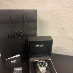 Grön kronografklocka från Hugo Boss - Stilren klocka från Hugo Boss med grön urtavla och silverfärgat armband i metall. Levereras i originalask med tillhörande påse och manual samt länk eftersom jag förkortat klockan. Perfekt accessoar för dig som gillar en snygg och lyxig känsla! 