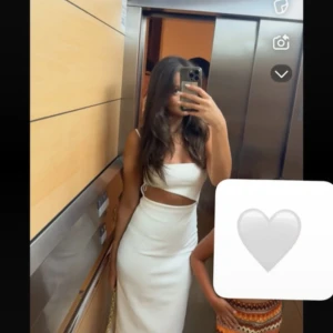 Vit långklänning med cut out-detalj - Säljer en stilren vit långklänning med smala axelband och snygg cut out-detalj i midjan. Klänningen har figurnära passform och är perfekt för dig som vill sticka ut med en modern och trendig look. Materialet känns mjukt och följsamt mot kroppen.