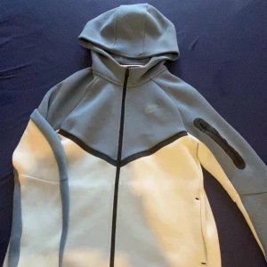 Nike blå och vit hoodiejacka XL - Nike hoodiejacka i blått och vitt med hel dragkedja och huva. Jackan har svart detalj längs dragkedjan och ärmarna, samt diskret Nike-logga på bröstet. Tillverkad i mjukt material, perfekt för chill dagar eller när du vill ha en sportig look.