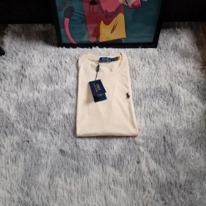 Vit t-shirt från Polo Ralph Lauren - Snygg vit t-shirt från Polo Ralph Lauren med klassisk logga broderad på bröstet. Enkel och stilren design med rund halsringning. Perfekt basplagg för en clean look.