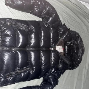  Mörkblå/svart Moncler pufferjacka - Snygg mörkblå pufferjacka när det är ljust men svart när det är mörkt från Moncler äkta men finns ingen påse eller kvitto därför säljer så billigt allt funkar som det ska alla nfc med glansig finish och huva. Jackan har flera dragkedjeförsedda fickor och klassisk quiltad design.  Ger den extra värme i vintern och har coola detaljer som märkets logga och serietidningsetikett på insidan. Fråga gärna om mer bilder eller om jackan privat
