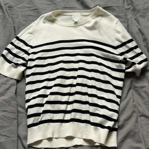 Randig kortärmad tröja från H&M - vit och svart randig tröja från H&M med korta ärmar och rund halsringning. Tröjan är stickad i mjukt material och har en klassisk, avslappnad passform. Perfekt för en stilren look under vår och sommar. Tröjan är använd cirka 2 gånger 