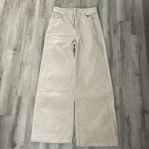 Beiga vida manchesterbyxor - Snygga beiga manchesterbyxor med breda ben och hög midja. Byxorna har klassiska fickor fram och bak, bälteshällor och stängs med knapp och dragkedja. Perfekta för en chill och trendig look.