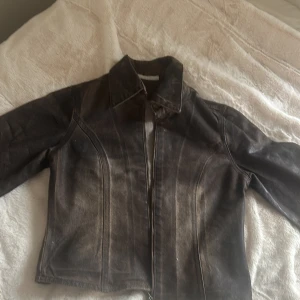 Brun skinnjacka med dragkedja - Snygg brun skinnjacka med klassisk krage och markerade sömmar. Jackan har dragkedja framtill och knappdetalj vid ärmslut. Modellen är figursydd och har en cool vintagekänsla. Perfekt för dig som vill ha en edgy look.